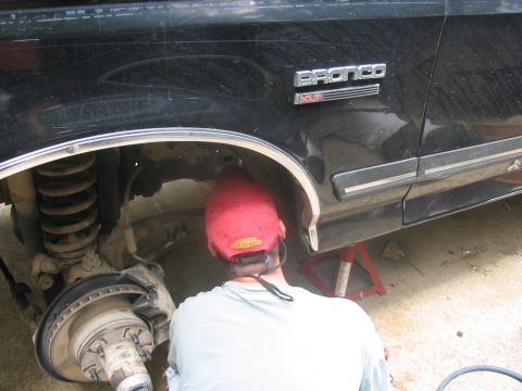 1988 Ford Bronco - A person works on the front suspension of a black Ford Bronco XL, which is supported by a jack stand.