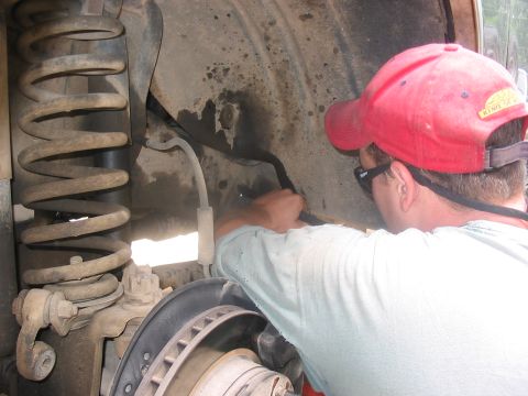 1988 Ford Bronco - A person works on the suspension of a vehicle, focusing on the wheel well area.