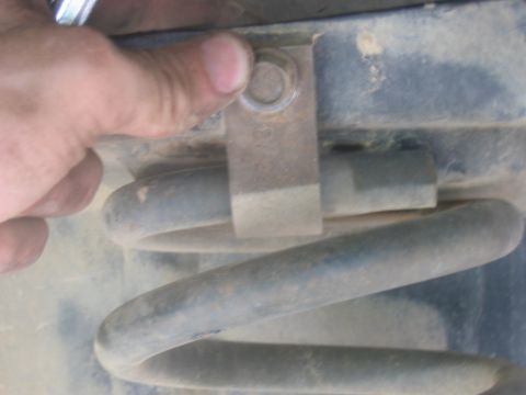 1988 Ford Bronco - A hand is shown adjusting a bolt on a suspension bracket near a coil spring.
