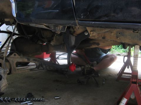 1988 Ford Bronco - A person works on the suspension of a vehicle lifted on jack stands, with tools scattered nearby.