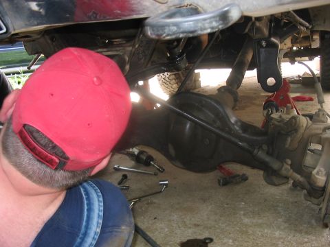 1988 Ford Bronco - A person works on the undercarriage of a vehicle, with tools and a jack visible.