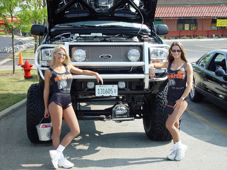 Black lifted Ford with raised hood and chrome grille guard, two women in Hooters tops standing beside it