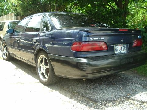 1993 Ford Taurus - This dark blue 1993 Ford Taurus sedan is viewed from the rear 3/4 angle, showing its distinctive taillights and spoiler.