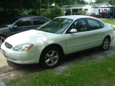2003 Ford Taurus - A white 2003 Ford Taurus sedan is parked in a driveway next to another car.