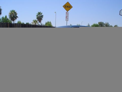 1993 Ford Taurus - A dark sedan is partially visible behind a wooden fence, with an 'END' traffic sign overhead.