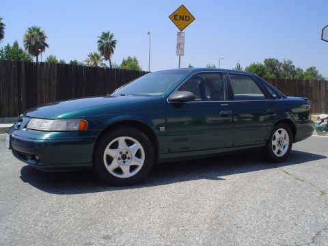 1993 Ford Taurus - Dark green 1993 Ford Taurus sedan parked on asphalt with a wooden fence and palm trees in the background.