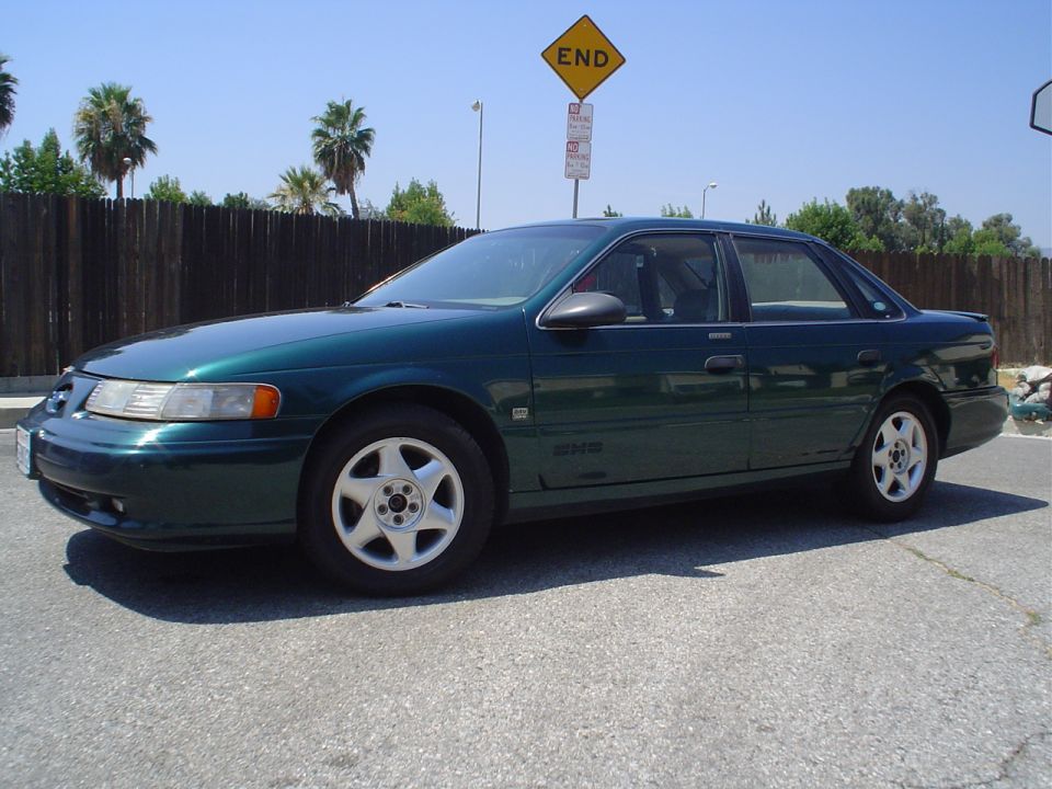 1993 Ford Taurus sedan, dark green, parked outdoors. Side view shows the front and rear wheels, doors, and windows