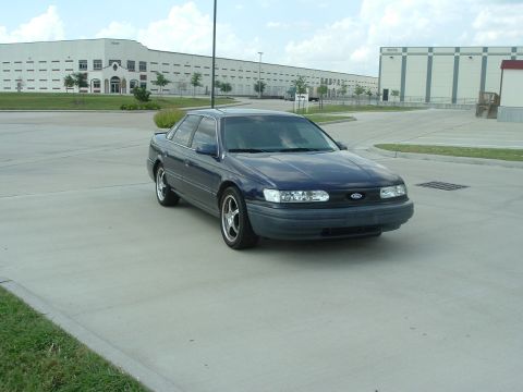 1993 Ford Taurus - Sedan parked in a lot with industrial buildings in the background.