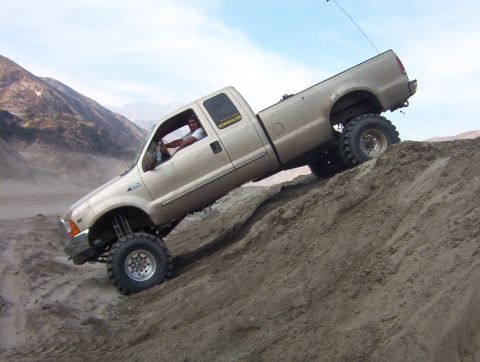 2000 Ford F-450 - A gold Ford F-450 truck navigates a steep dirt incline under a hazy sky.