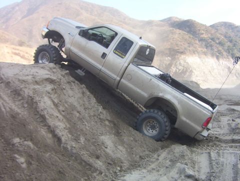 2000 Ford F-450 - A lifted 2000 Ford F-450 with large tires navigates a steep dirt incline, kicking up dust.