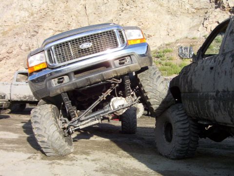 2000 Ford F-450 - A modified Ford Super Duty truck is shown at an extreme angle, interacting with another dirty vehicle.