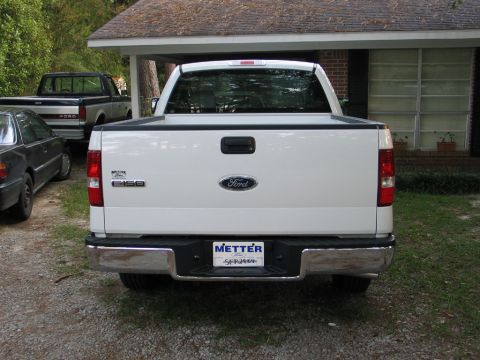 2004 Ford F-150 - This white Ford F-150 pickup truck is parked in a driveway next to a house, with other vehicles nearby.