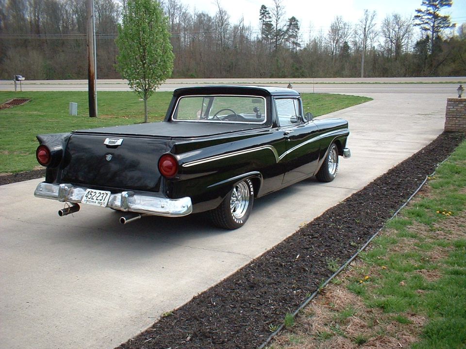 Black 1957 Ford Ranchero, rear 3/4 view, chrome wheels and dual exhaust on driveway