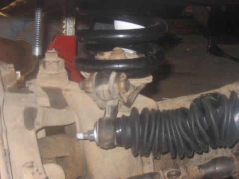 1988 Ford Bronco - Detail shot of vehicle suspension components, including a coil spring and tie rod end, with a jack visible. The Supermotors.net logo is in…
