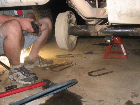 1988 Ford Bronco - Underneath a vehicle, a person works on the rear axle, with tools and parts scattered around.