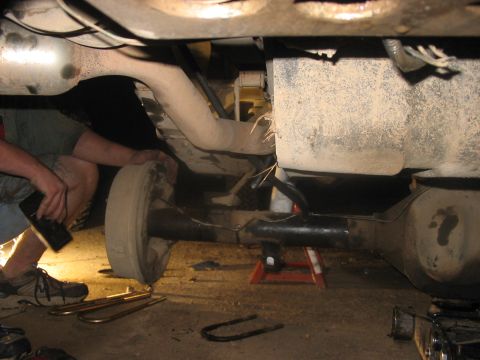 1988 Ford Bronco - Mechanic works on the undercarriage of a vehicle, focusing on the rear axle and exhaust system.
