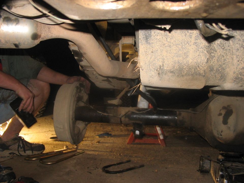 Undercarriage of a vehicle being worked on, showing a rear axle, exhaust pipe, and a mechanic's hands