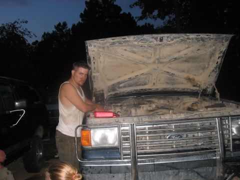 1988 Ford Bronco - A man is working on the engine of a dirty truck, with another vehicle visible in the background.