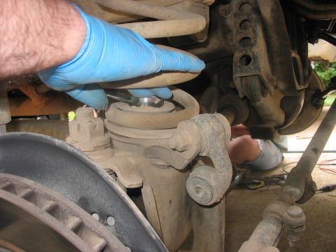 1988 Ford Bronco - Mechanic works on the suspension of a vehicle, focusing on a spring and bolt assembly.