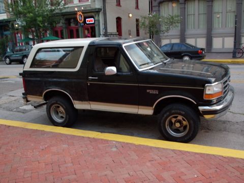 1993 Ford Bronco - A black and white Ford Bronco is parked on a street with a yellow curb.