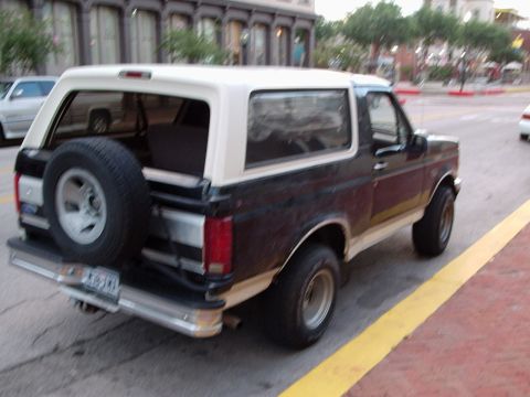 1993 Ford Bronco - This two-tone Ford Bronco is seen from the rear, parked on a street with buildings in the background.