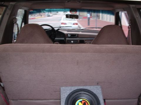 1993 Ford Bronco - The interior of a vehicle shows the dashboard and a view of the street through the windshield, with a subwoofer in the back.