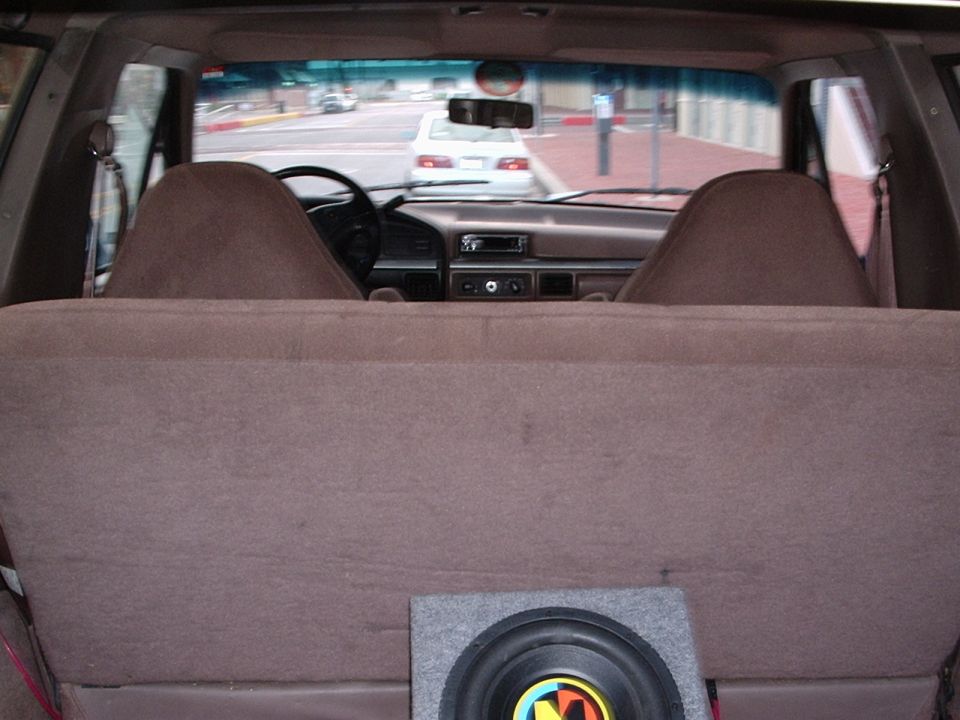View from back seat looking forward at dashboard and street scene outside. Subwoofer visible in cargo area
