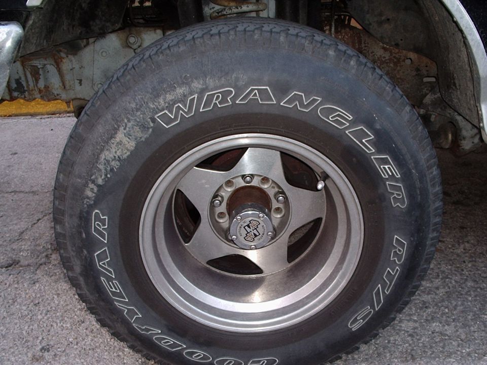 Close-up of a Goodyear Wrangler RT/S tire on a five-spoke alloy wheel, showing rust on the vehicle's frame