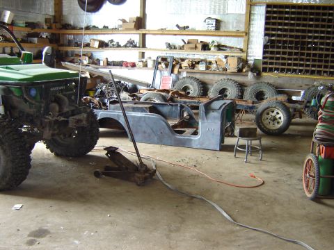 1992 Ford Bronco - A disassembled Jeep CJ-6 body and chassis sits in a workshop, with a green Suzuki Samurai partially visible.