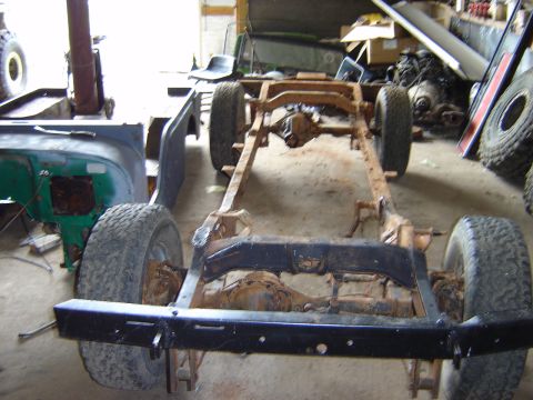1992 Ford Bronco - The frame and axles of a Jeep CJ-6 are visible, with parts of the body and other vehicles in the background.