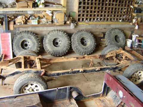 1992 Ford Bronco - A disassembled vehicle frame sits in a workshop, surrounded by spare tires and parts.