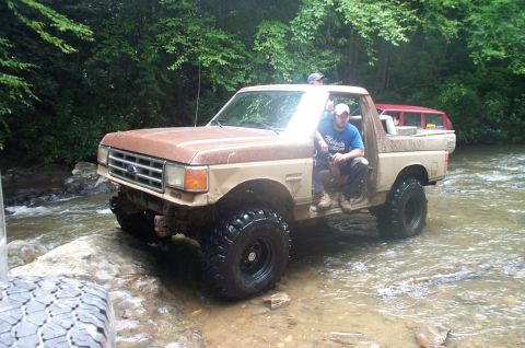 1987 Ford Bronco - A 1987 Ford Bronco navigates a rocky stream bed, with another vehicle visible in the background.