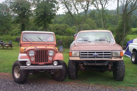 1987 Ford Bronco - A 1987 Ford F-Series truck is parked next to a red Jeep with a wooded background.