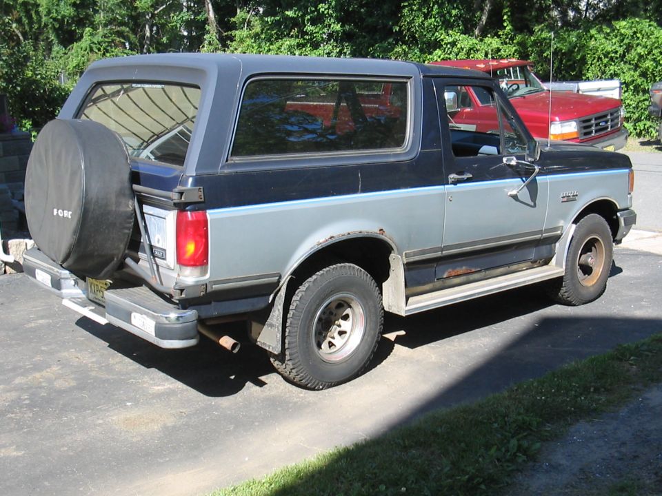 Two-tone blue and gray Ford Bronco with a rear-mounted spare tire, seen from the rear-left