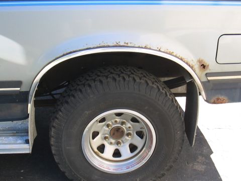 1979 Ford Bronco - Close-up of a truck's rear wheel well shows rust and a tire with chrome trim.