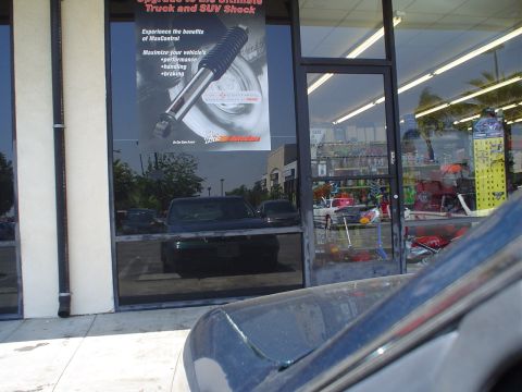 1993 Ford Taurus - Reflection of vehicles in a storefront window, with a poster for truck and SUV shocks visible.