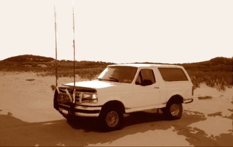 1996 Ford Bronco - A white 1996 Ford Bronco is parked in a sandy, desert environment with two tall antennas on its roof.
