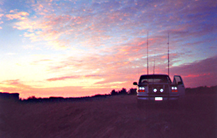 1996 Ford Bronco - A pickup truck is parked in a field with fishing rods in the bed during a colorful sunset.