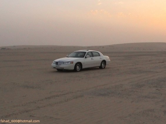 White Lincoln Town Car parked on desert sand with tire tracks, distant 3/4 front view