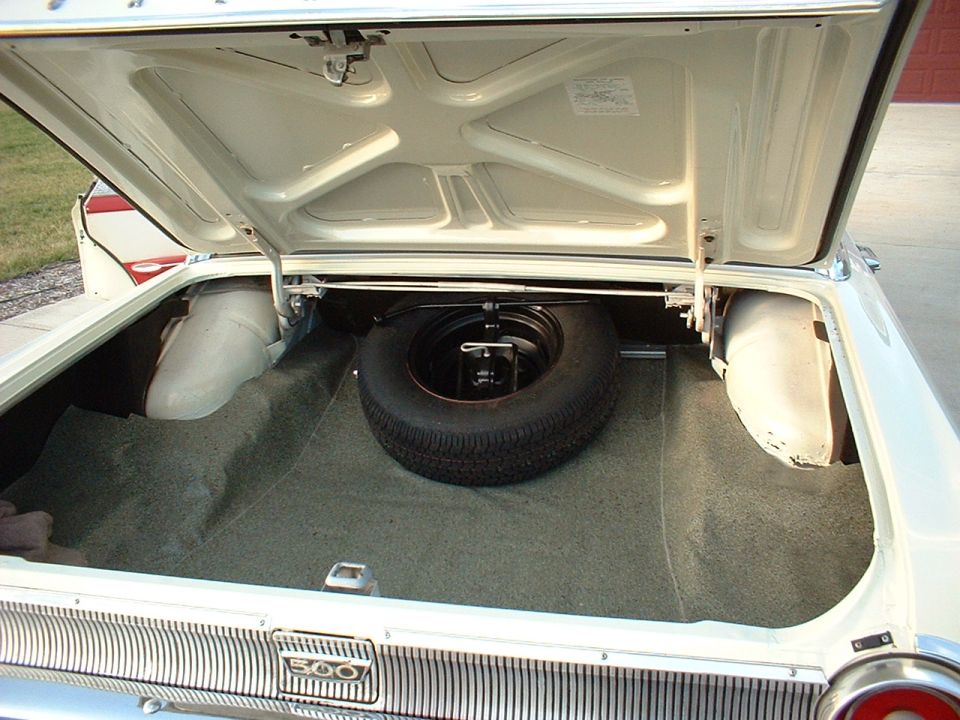 Open trunk of a white Ford Galaxie 500 with spare tire and green trunk carpet