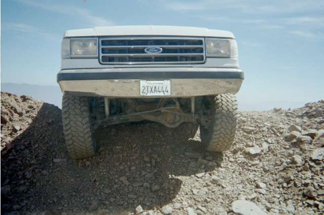 Front low view of a lifted white Ford truck showing solid axle and CA plate