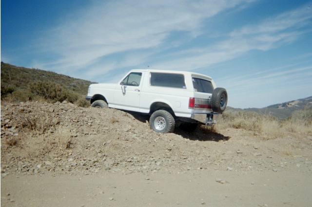 White Ford Bronco descending a dirt hill, rear three-quarter view