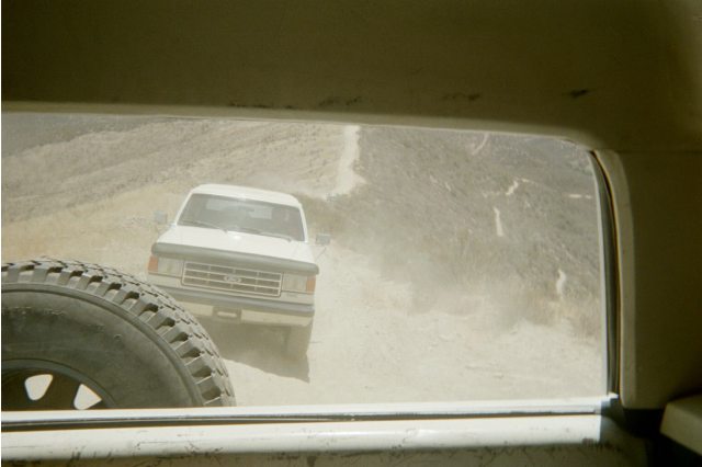 White Ford truck on a dusty trail seen through another vehicle's window