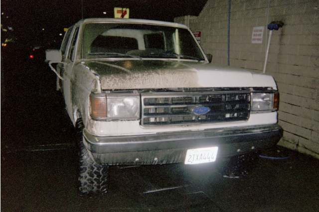 White Ford pickup with lift kit parked at night near a block wall