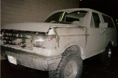 1990 Ford Bronco - Front three-quarter view of a white Ford Bronco SUV heavily caked in dried mud, shot at night by a wall.