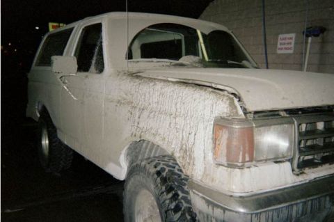 1990 Ford Bronco - Passenger side of a white Ford Bronco caked in dried mud at night near a car-wash bay with a posted sign.