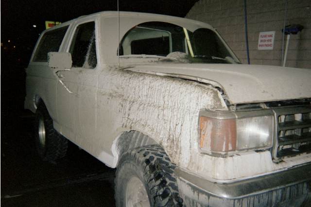 Side of a white Ford Bronco SUV plastered with dried mud at night