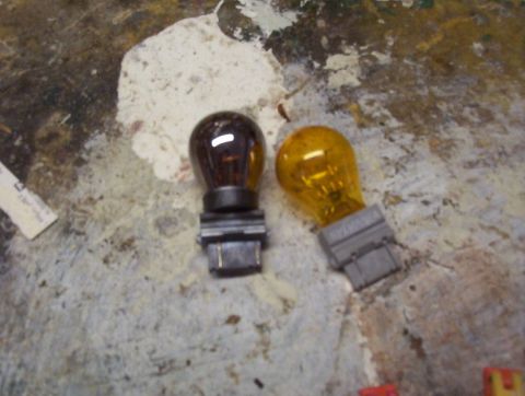 1989 Ford Bronco - Two automotive light bulbs, one amber and one brown, are shown on a workbench.