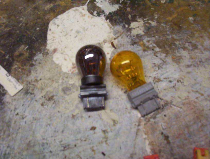 Two automotive light bulbs, one amber and one brown, on a textured surface