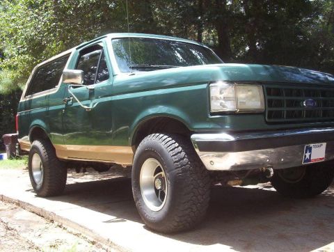 1989 Ford Bronco - This lifted 1989 Ford Bronco is parked outdoors on a paved surface with trees in the background.